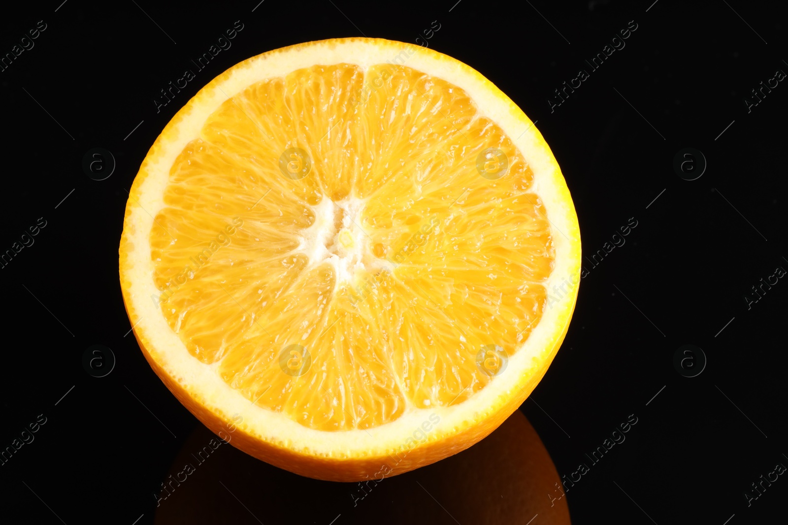 Photo of Half of fresh orange on black mirror surface, closeup