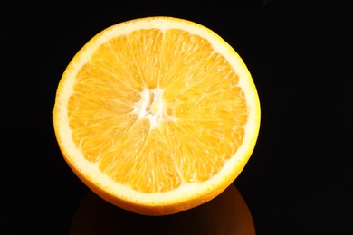 Photo of Half of fresh orange on black mirror surface, closeup