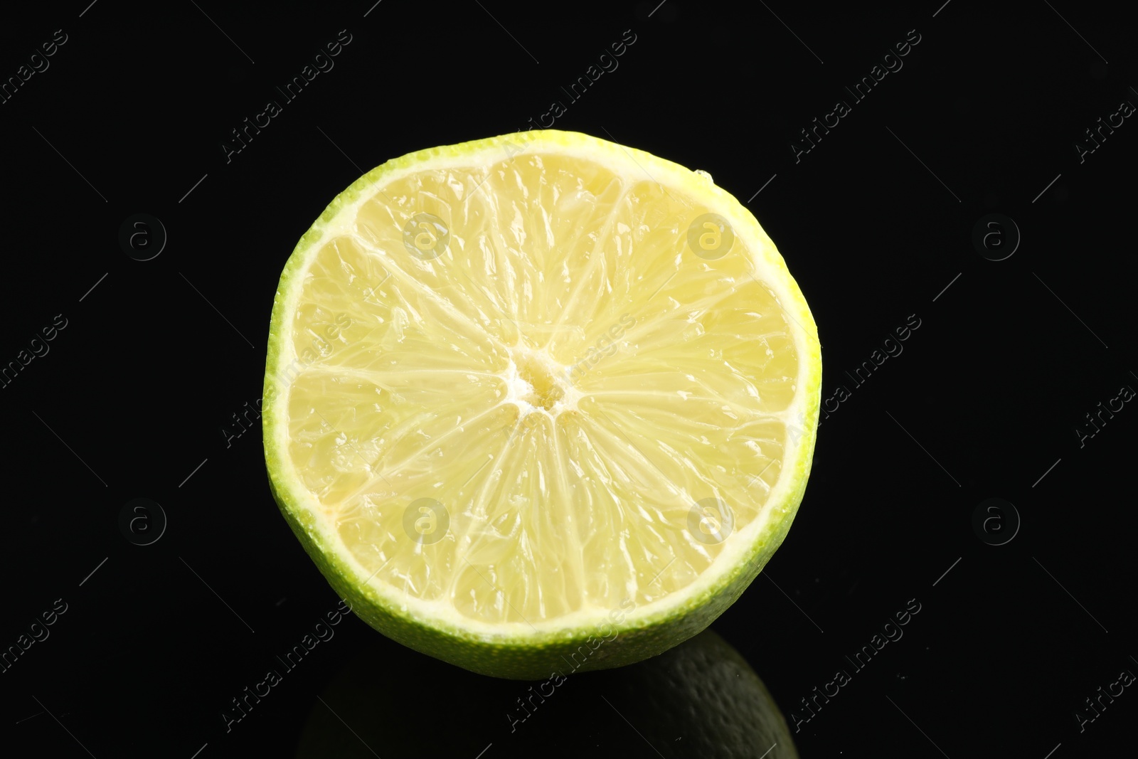 Photo of Half of fresh lime on black glass surface, closeup