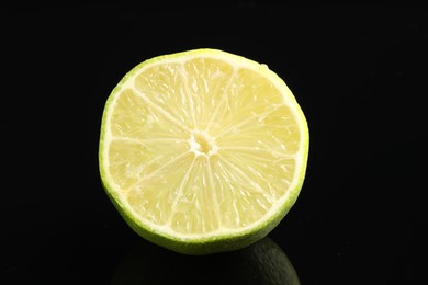 Photo of Half of fresh lime on black glass surface, closeup