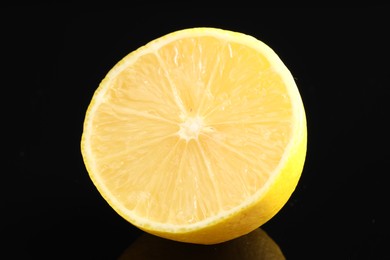 Photo of Half of fresh lemon on black glass surface, closeup