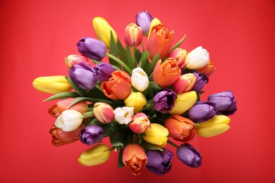 Photo of Bouquet of beautiful colorful tulips on red background, top view