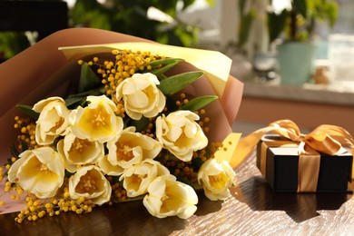 Photo of Bouquet with beautiful tulips, mimosa flowers and gift box on wooden table indoors