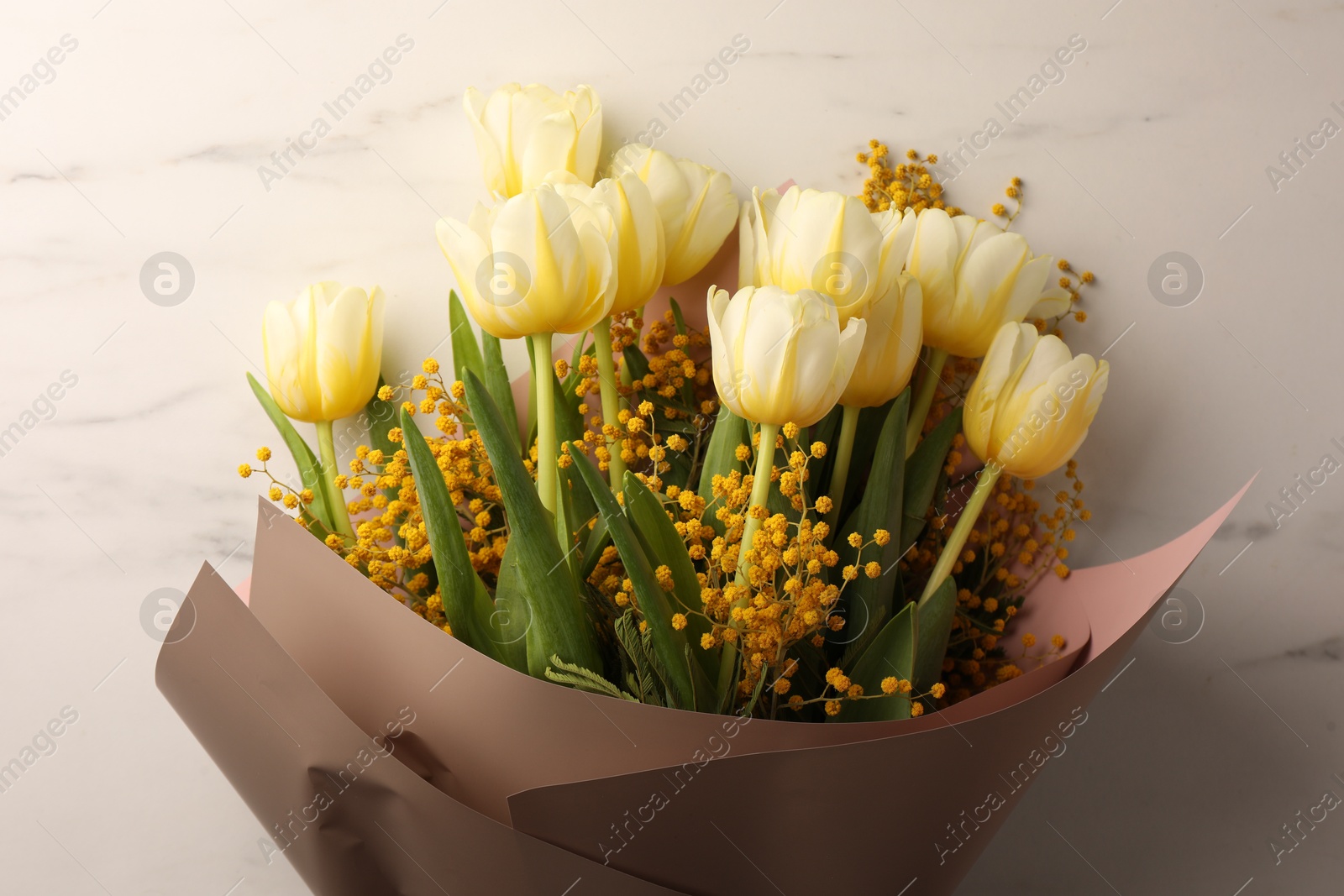 Photo of Bouquet with beautiful tulips and mimosa flowers on white marble table, top view