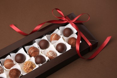 Photo of Box with delicious chocolate candies on brown table, closeup