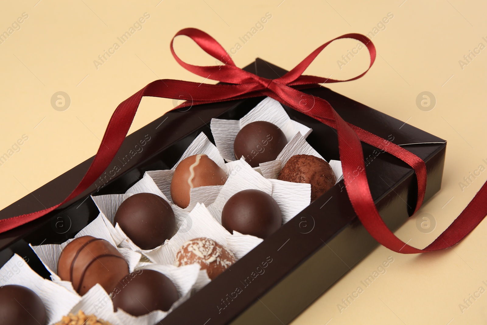 Photo of Box with delicious chocolate candies on beige table, closeup