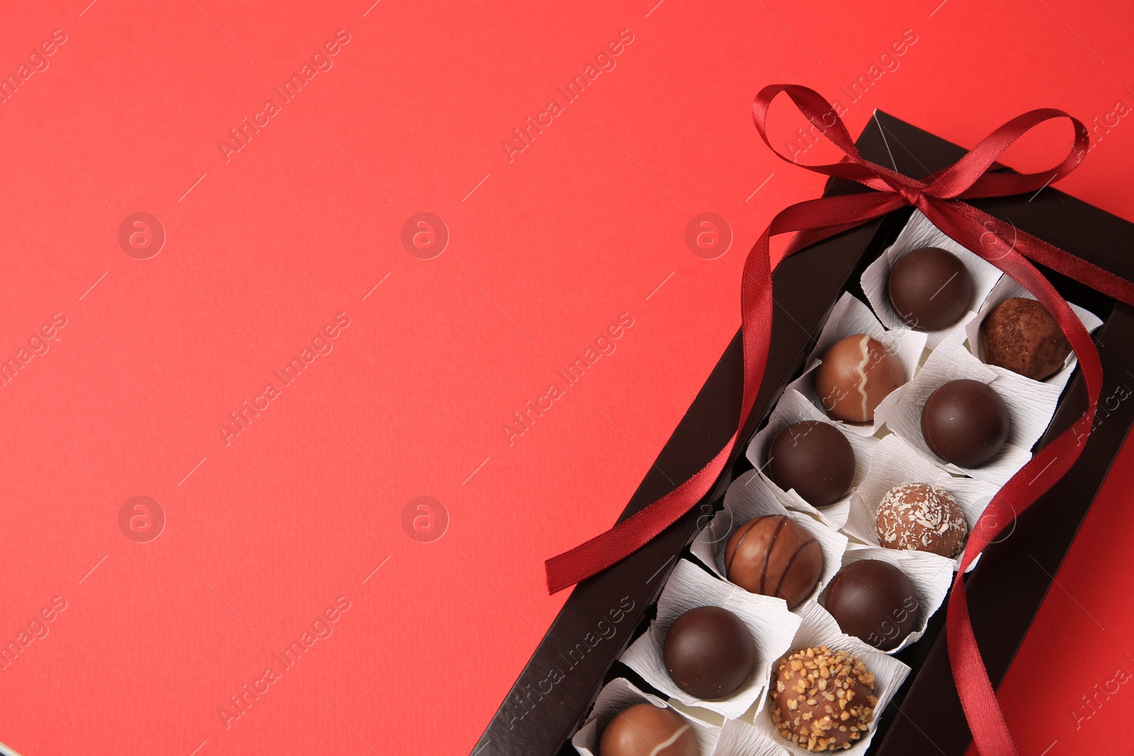 Photo of Box with delicious chocolate candies on red table, top view. Space for text