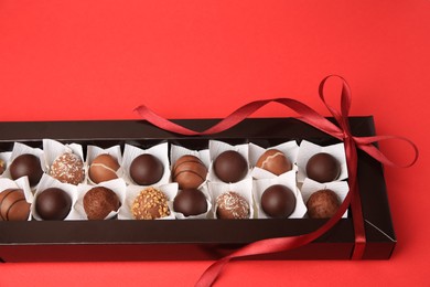 Photo of Box with delicious chocolate candies on red table, closeup