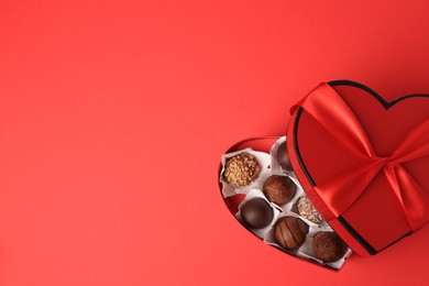 Photo of Heart shaped box with delicious chocolate candies on red table, top view. Space for text