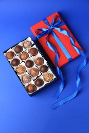 Photo of Box with delicious chocolate candies on blue background, flat lay