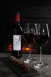 Photo of Red wine and chocolate truffles on gray table against fireplace