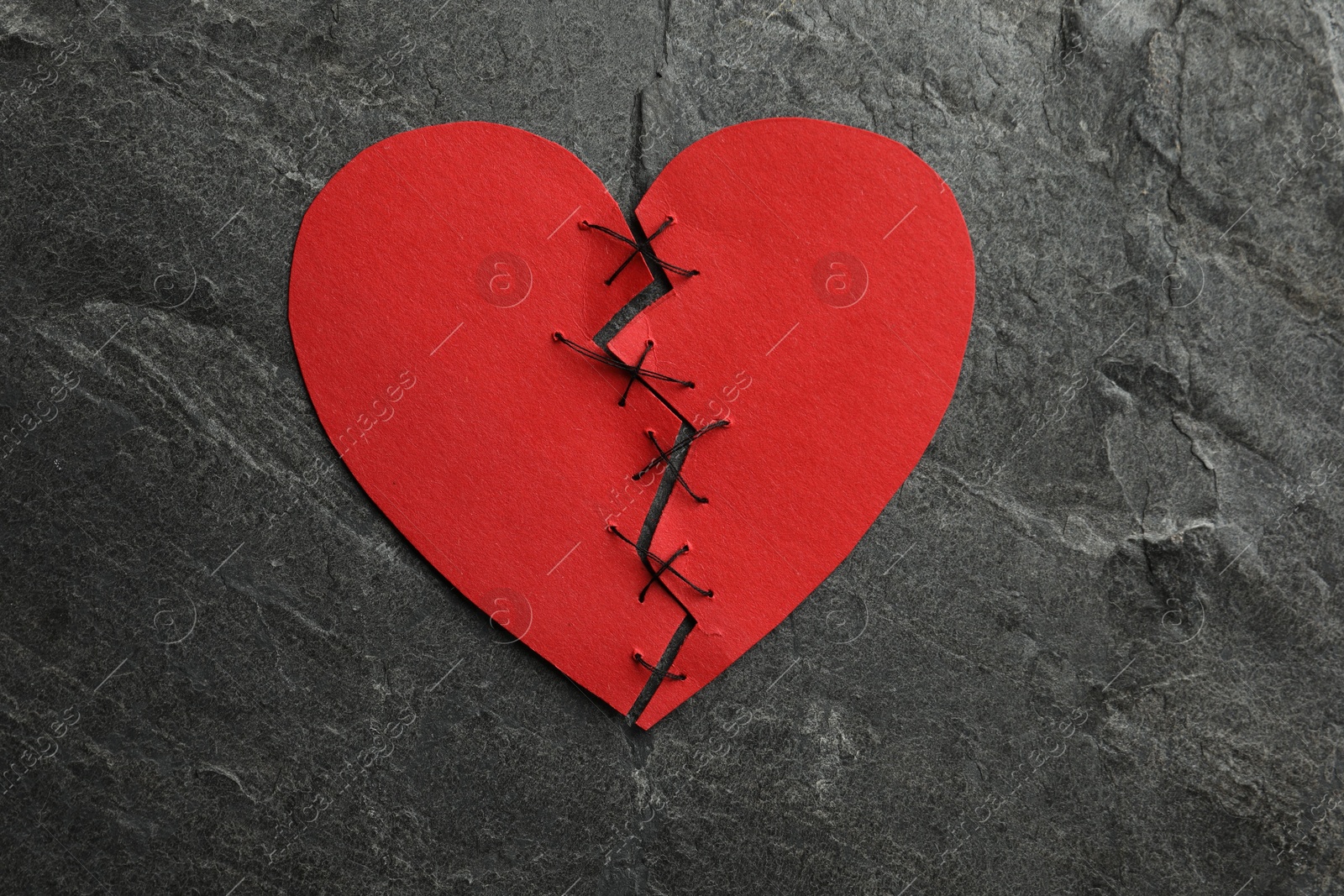 Photo of Broken heart. Torn red paper heart sewed with thread on dark grey table, top view