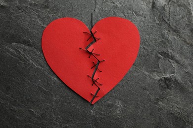 Photo of Broken heart. Torn red paper heart sewed with thread on dark grey table, top view