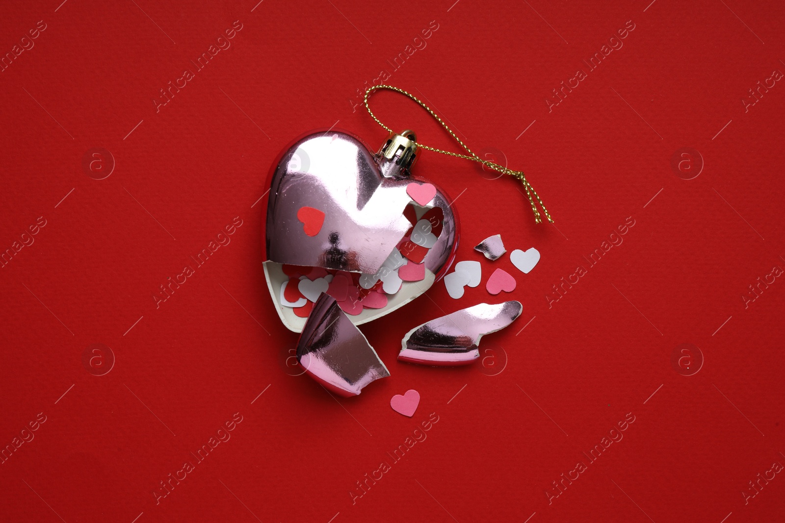 Photo of Crashed bauble in shape of heart with confetti on red background, top view. Broken heart