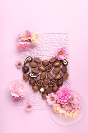 Photo of Heart made with delicious chocolate candies and beautiful flowers on pink background, flat lay