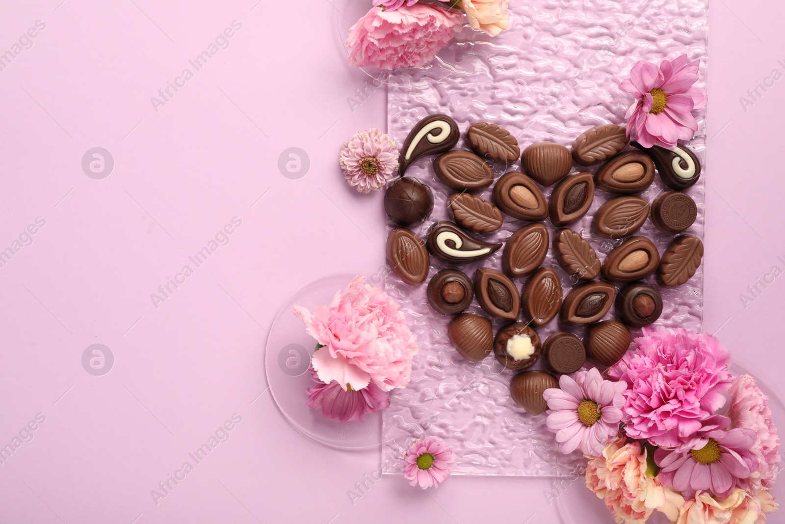 Photo of Heart made with delicious chocolate candies and beautiful flowers on pink background, flat lay. Space for text