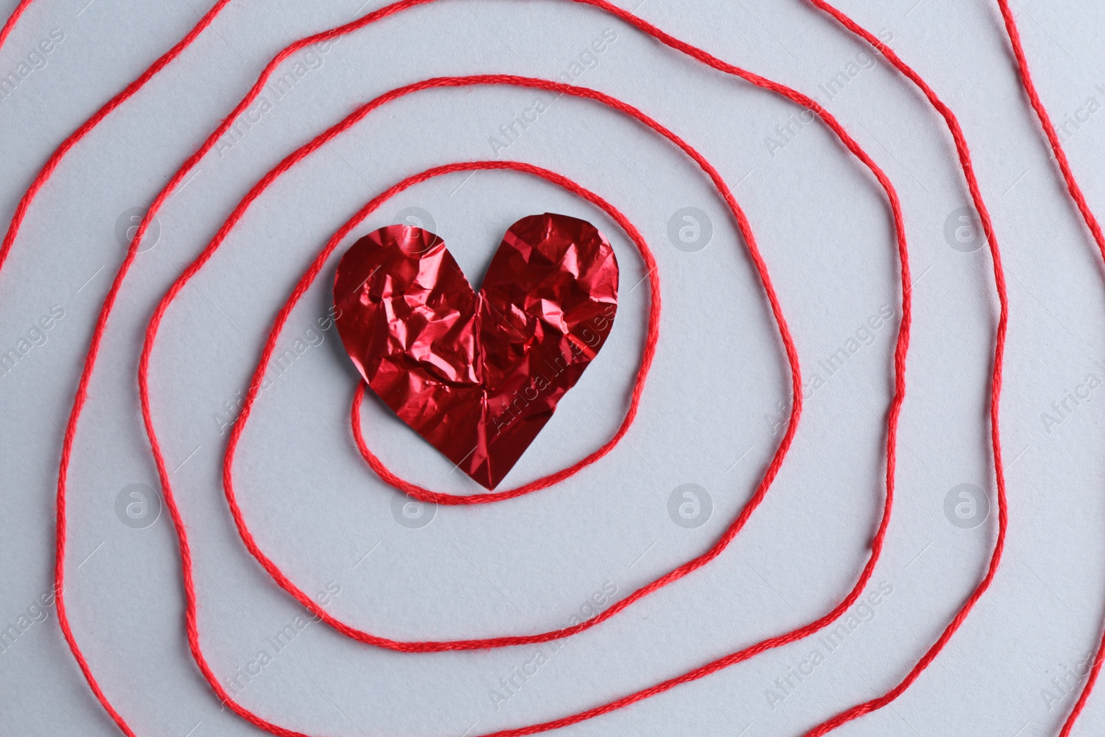 Photo of Red crumpled paper heart and thread on gray background, top view