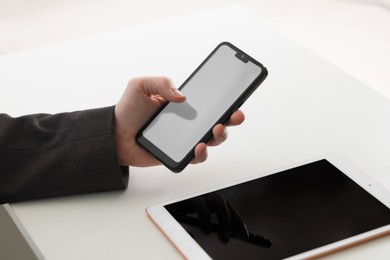 Photo of Businessman using smartphone near tablet at white table indoors, closeup. Modern technology