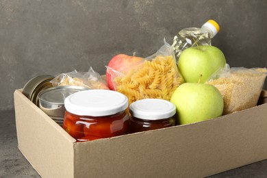 Photo of Different food products for donation in box on grey table, closeup