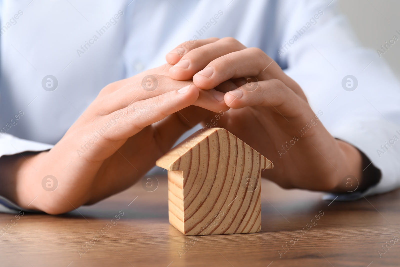 Photo of Real estate insurance. Man with wooden house figure at table, closeup