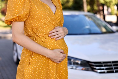 Photo of Pregnant woman near car outdoors, closeup. Space for text