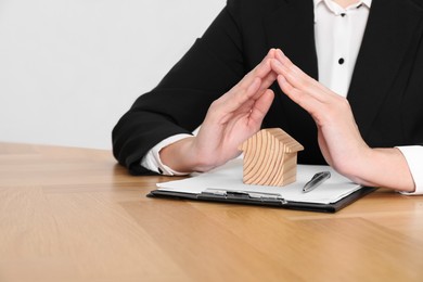 Photo of Property insurance. Real estate agent protecting wooden house figure at table indoors, closeup