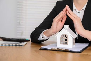 Photo of Property insurance. Real estate agent protecting house figure at wooden table indoors, closeup