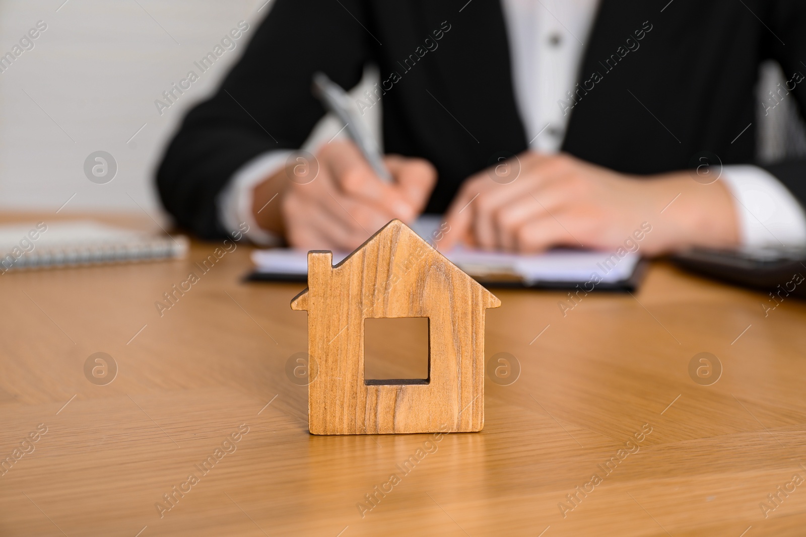 Photo of Property insurance. Real estate agent working at table indoors, focus on wooden house figure