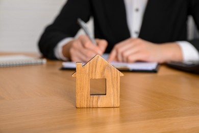 Photo of Property insurance. Real estate agent working at table indoors, focus on wooden house figure