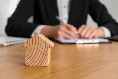 Photo of Property insurance. Real estate agent working at table indoors, focus on wooden house figure