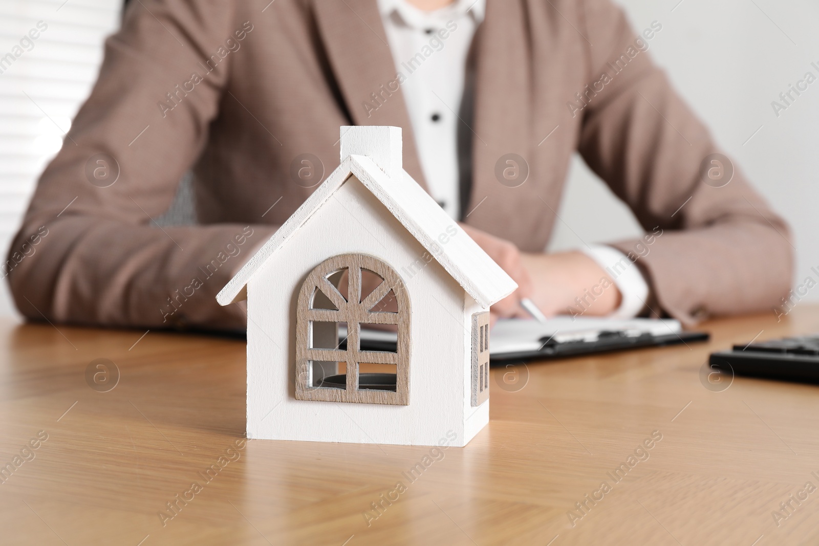 Photo of Property insurance. Real estate agent working at wooden table indoors, focus on house figure