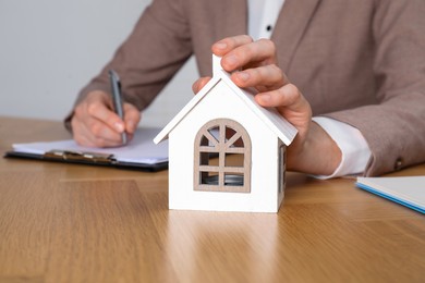 Photo of Property insurance. Real estate agent with house figure working at wooden table indoors, closeup