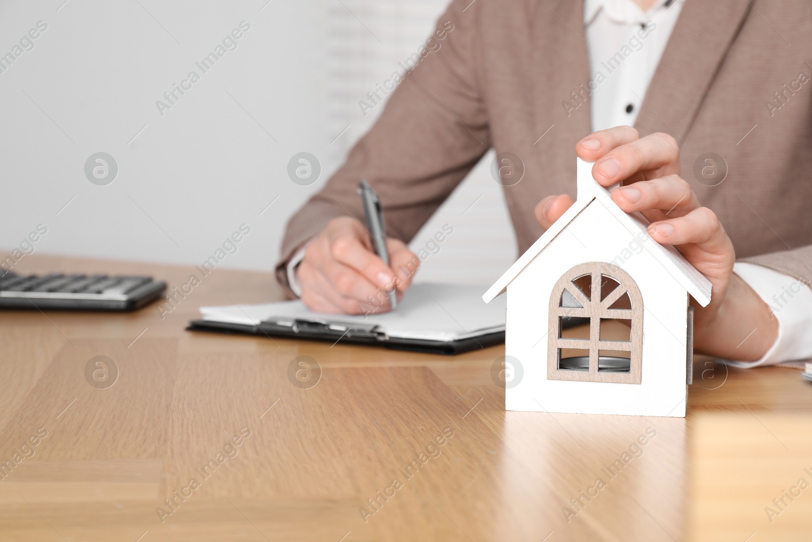 Photo of Property insurance. Real estate agent with house figure working at wooden table indoors, closeup