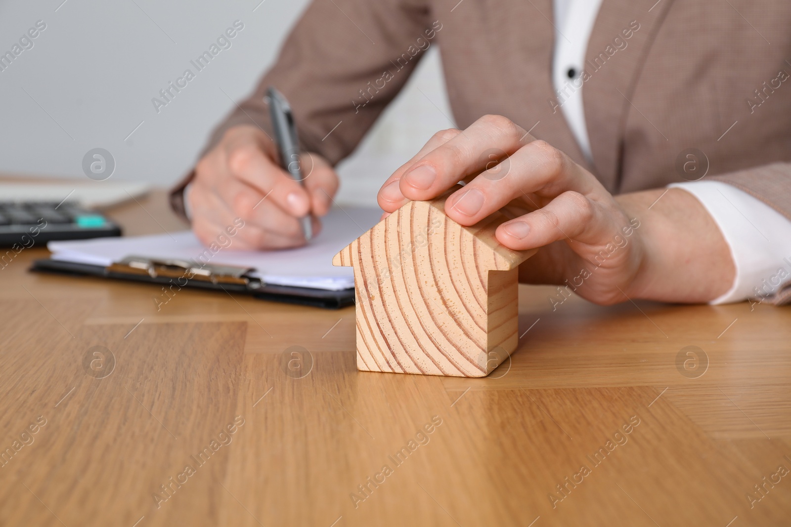 Photo of Property insurance. Real estate agent with house figure working at wooden table indoors, closeup