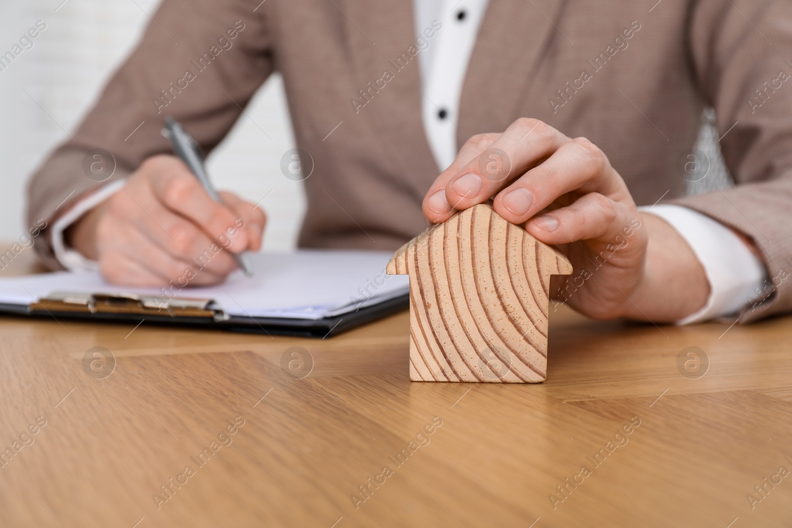 Photo of Property insurance. Real estate agent with house figure working at wooden table indoors, closeup