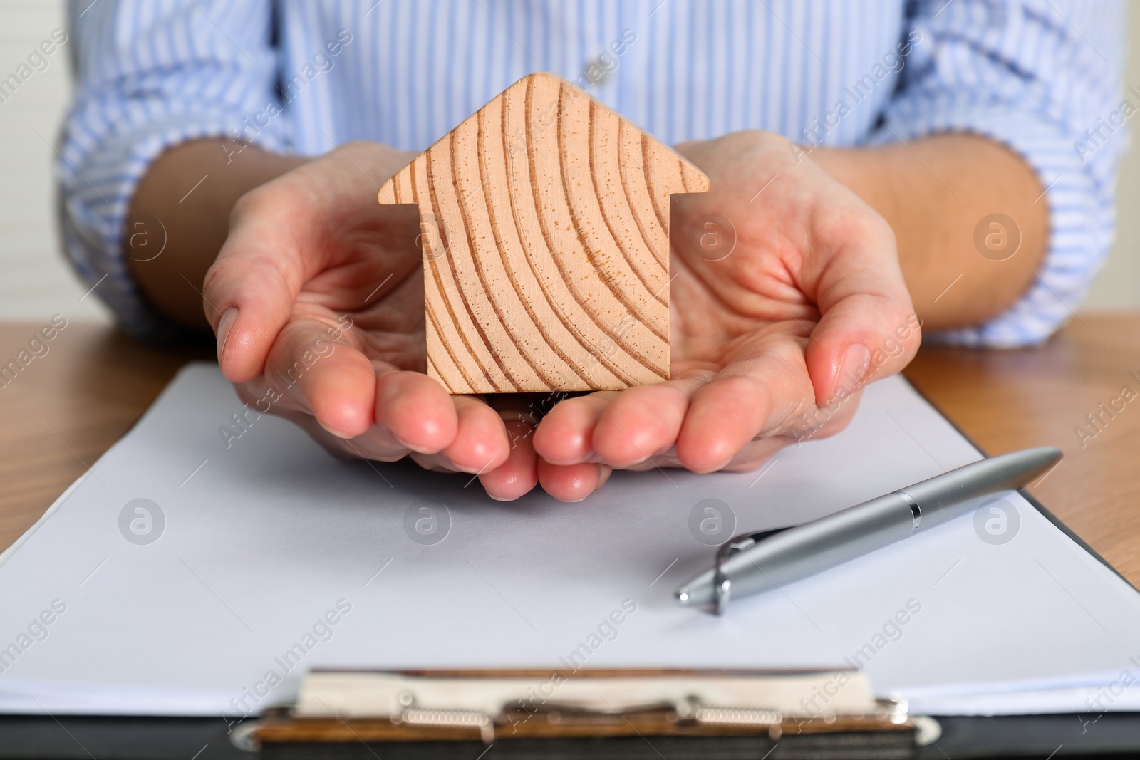 Photo of Property insurance. Real estate agent with wooden house figure at table indoors, closeup