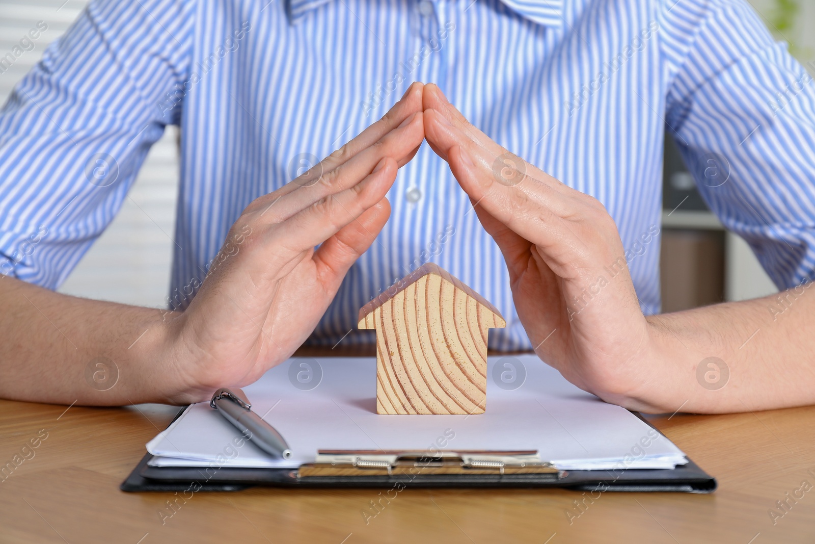 Photo of Property insurance. Real estate agent protecting wooden house figure at table indoors, closeup