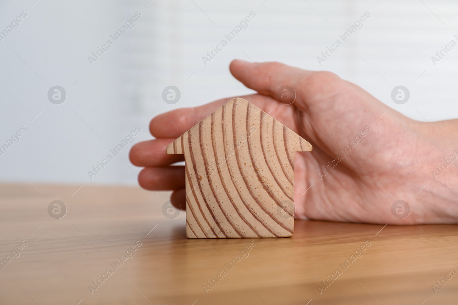 Photo of Property insurance. Real estate agent with wooden house figure at table indoors, closeup