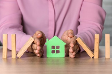 Photo of Property insurance. Real estate agent protecting house figure at wooden table indoors, closeup