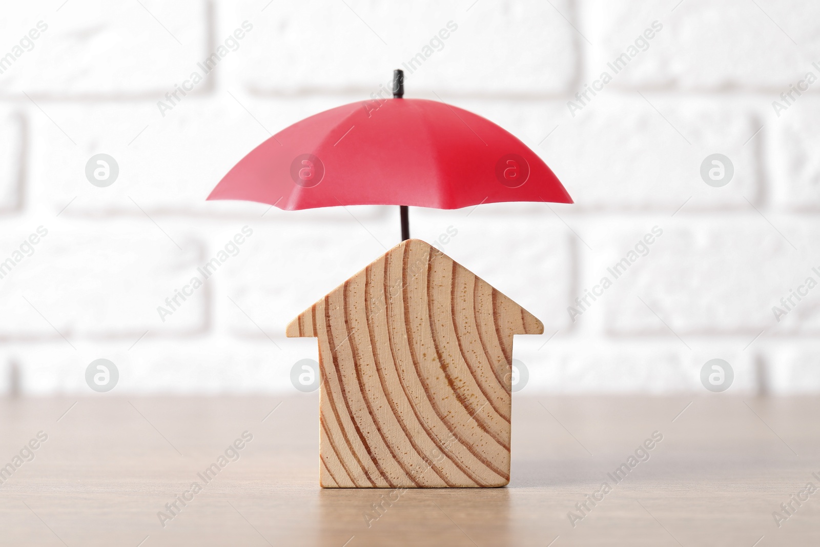 Photo of Property insurance. Wooden house figure and small umbrella on table indoors