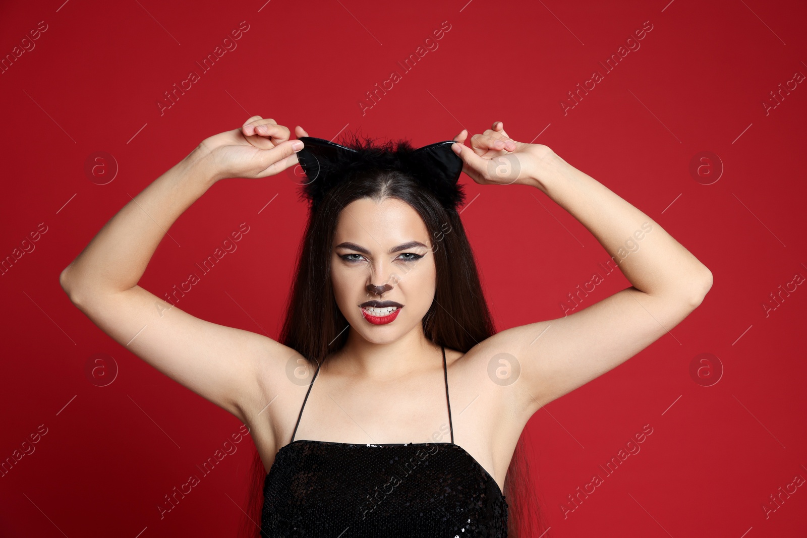 Photo of Beautiful woman with cat makeup and ears on red background