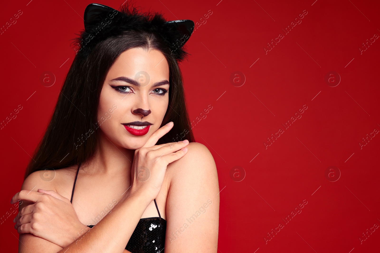 Photo of Beautiful woman with cat makeup and ears on red background. Space for text