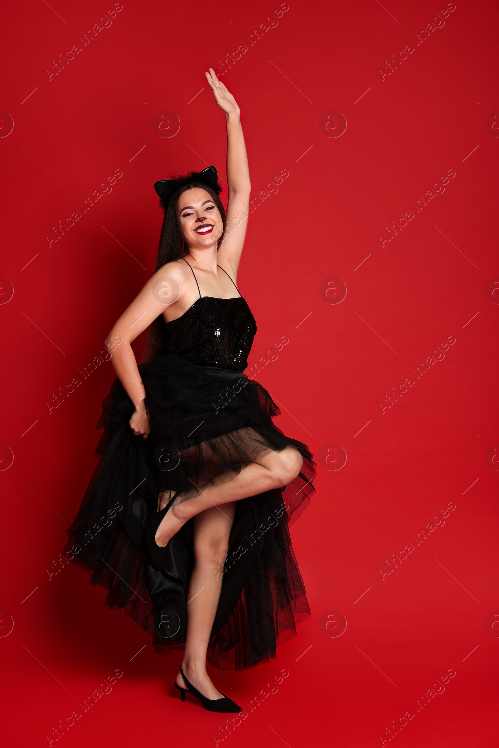 Photo of Woman with cat makeup and ears in beautiful dress on red background