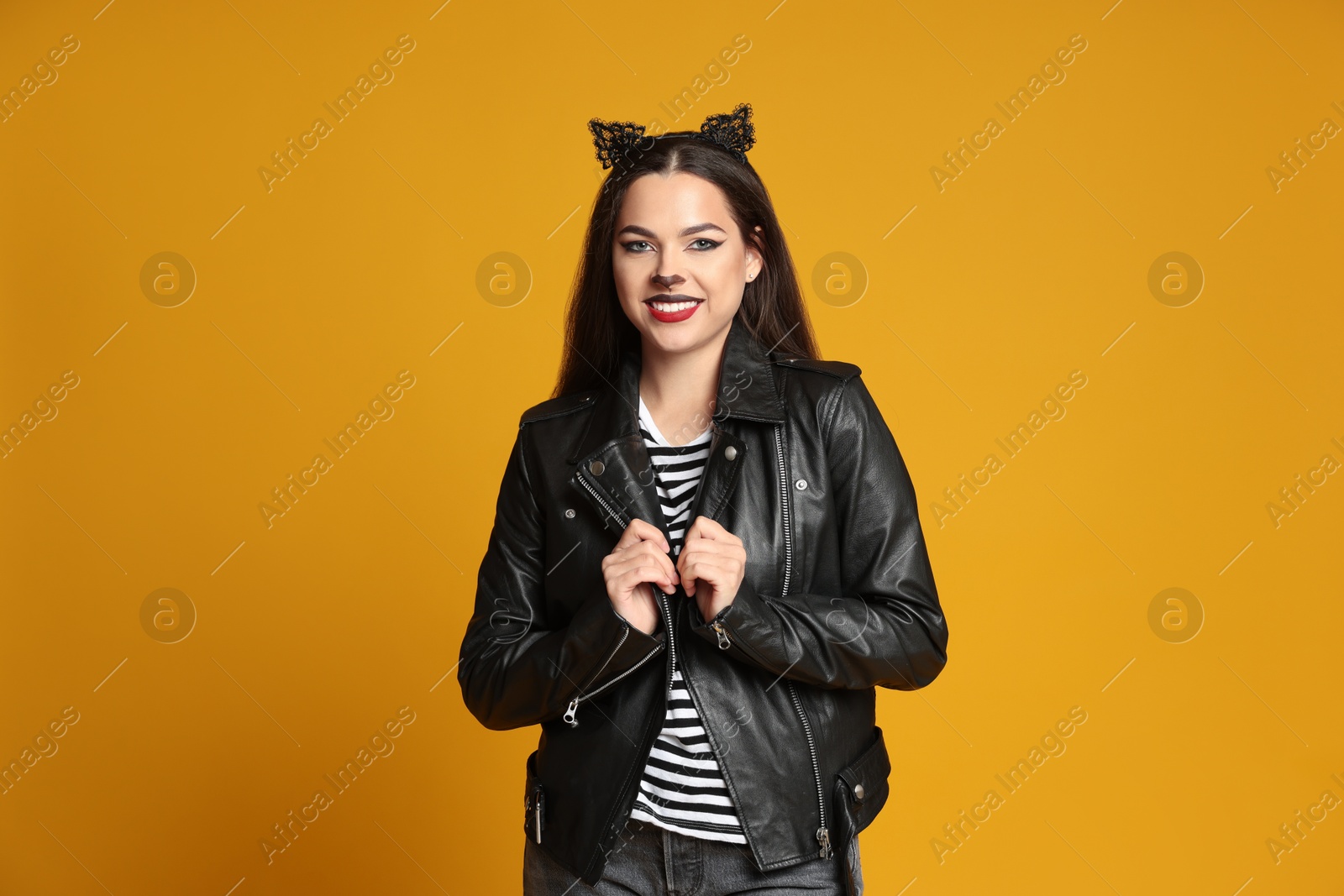 Photo of Woman with cat makeup and ears in leather jacket on orange background