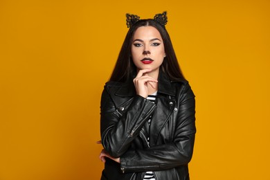 Photo of Woman with cat makeup and ears in leather jacket on orange background