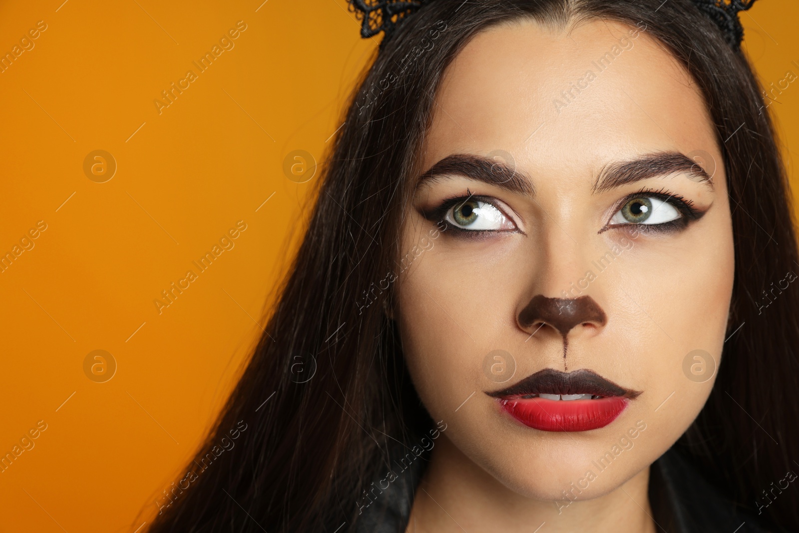 Photo of Woman with cat makeup and ears on orange background