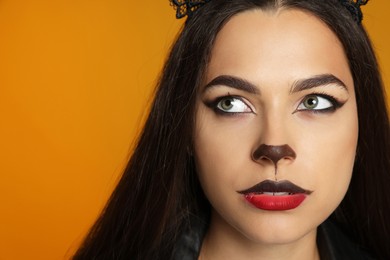 Photo of Woman with cat makeup and ears on orange background