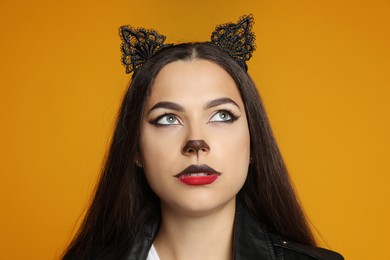 Photo of Woman with cat makeup and ears on orange background