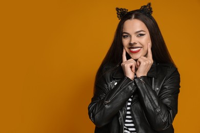 Photo of Woman with cat makeup and ears in leather jacket on orange background. Space for text