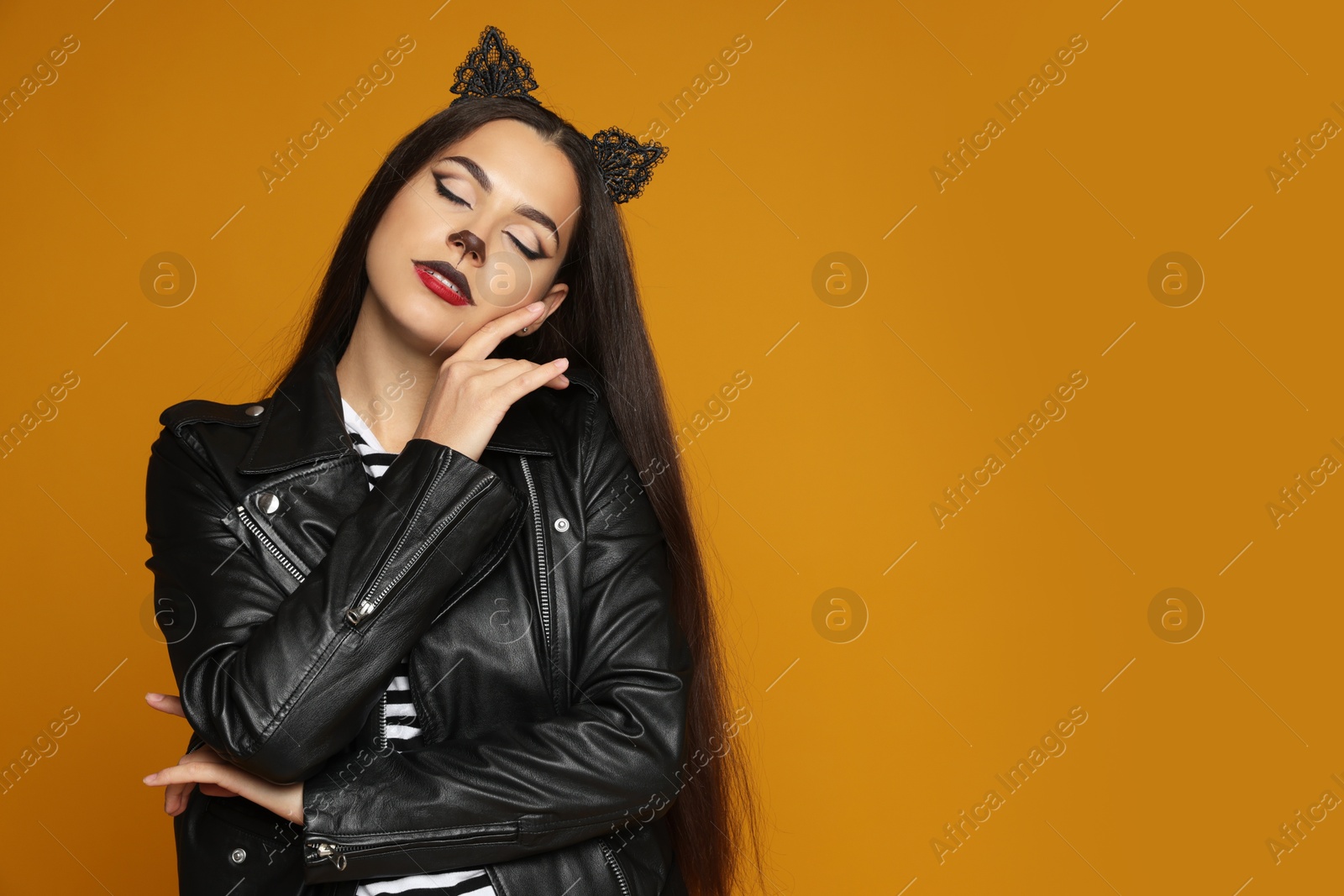 Photo of Woman with cat makeup and ears in leather jacket on orange background. Space for text